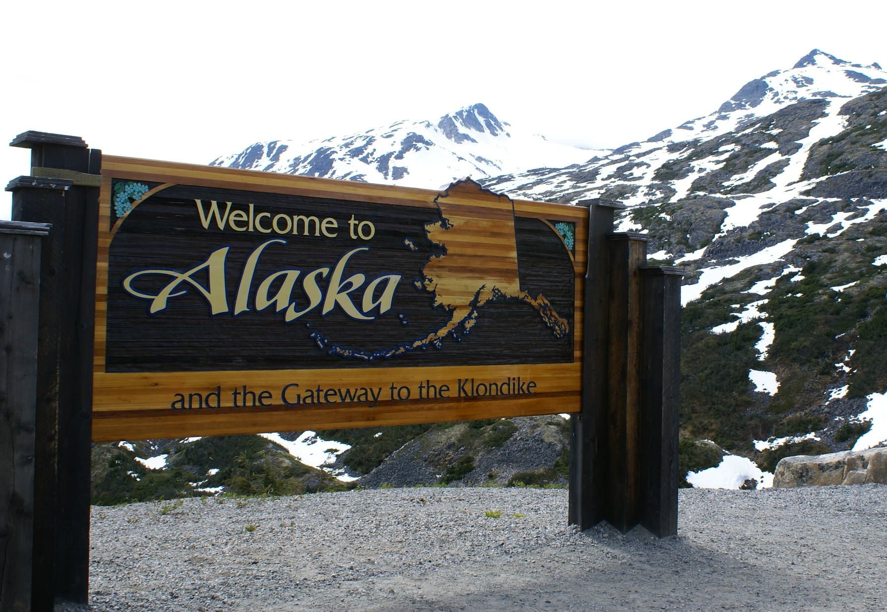 Welcome to Alaska sign with mountains in the background.