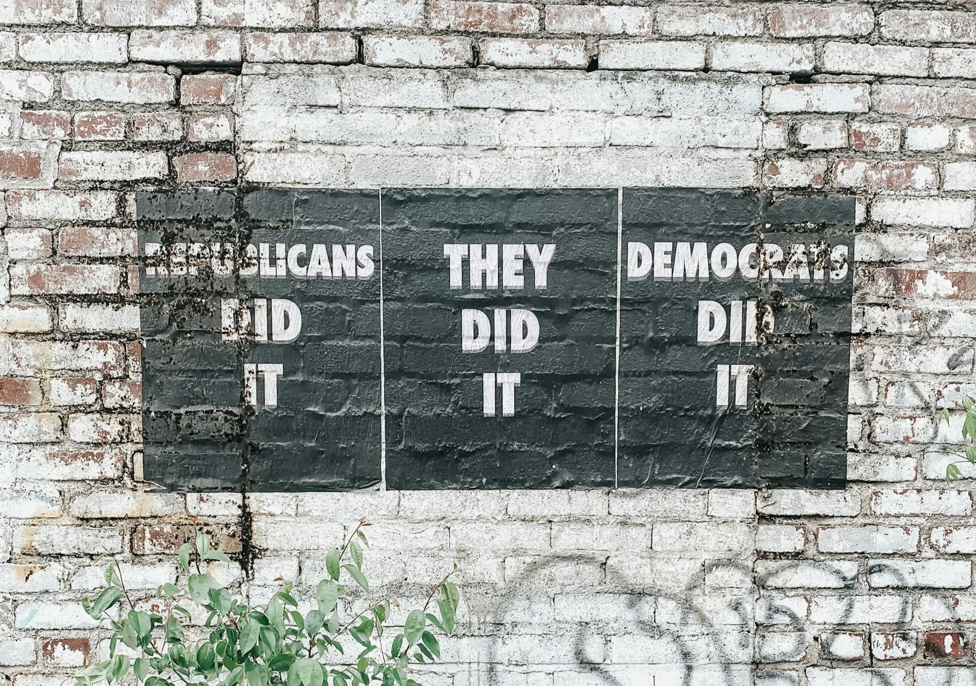 Brick wall with a sign that says Republicans did it on the left, They did it in the middle, and Democrats did it on the right. 